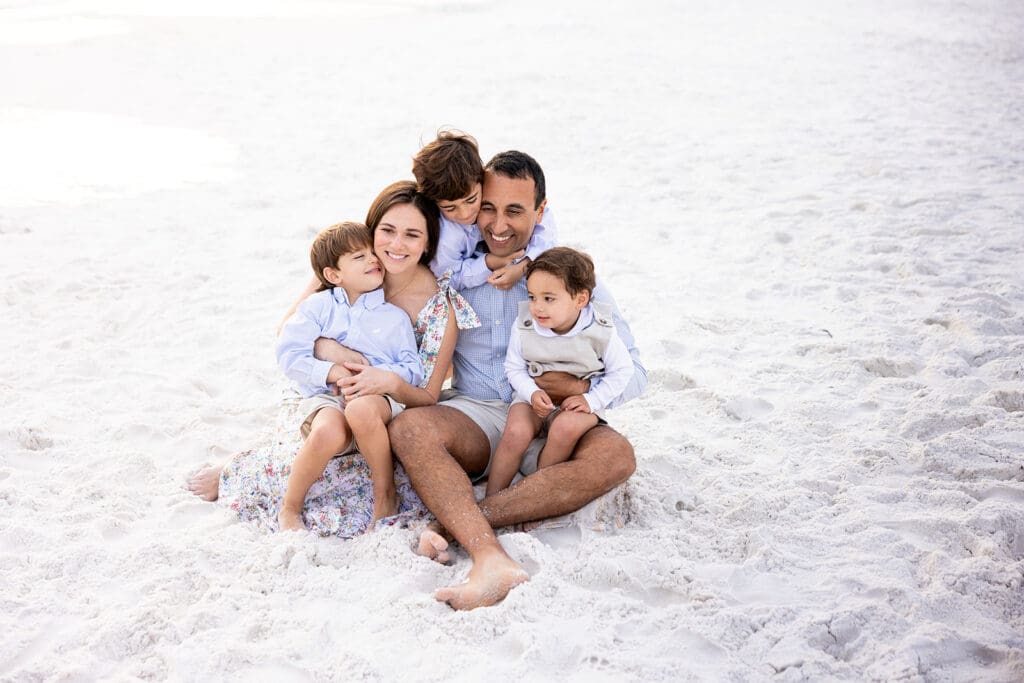 family sitting in the sand cuddling together 