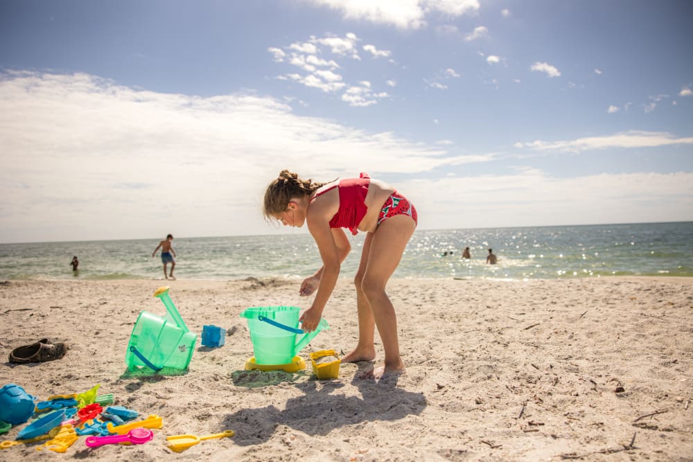 Child playing in the sand with buckets and shovels on a sunny Gulf beach during a relaxed day trip to Sanibel Island, with families enjoying the water in the background.